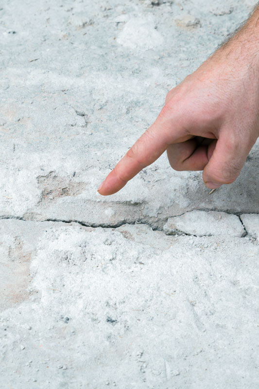 Hand, die auf einen Riss im Beton zeigt.