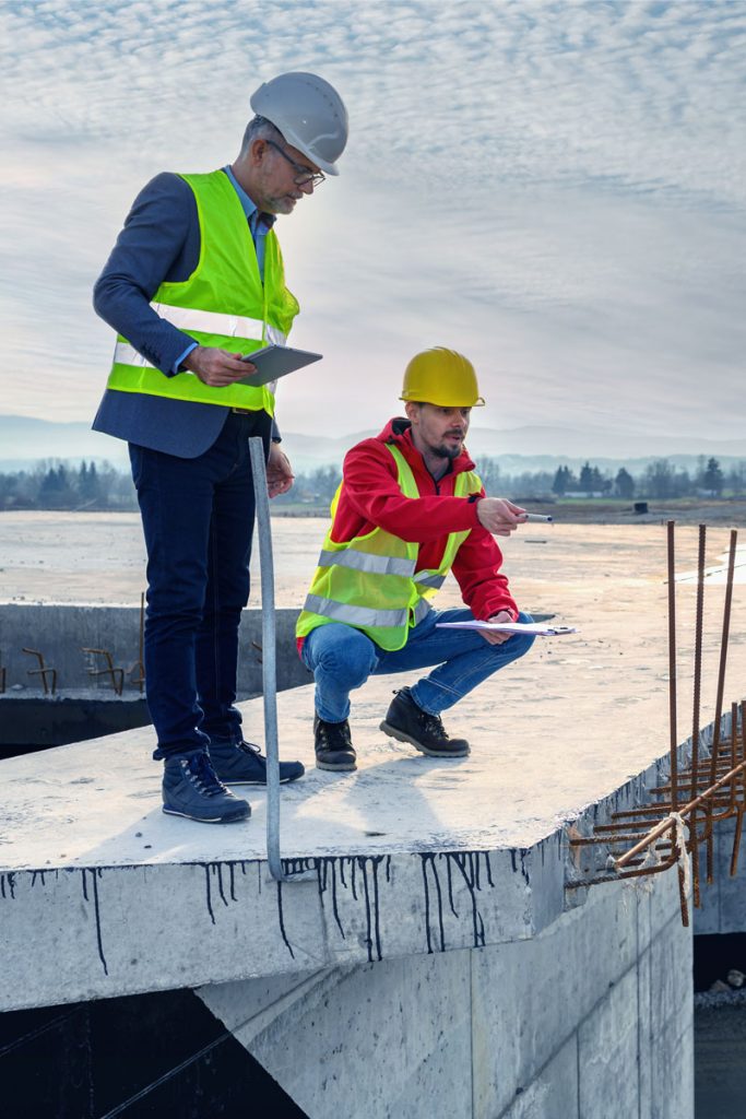 Zwei Personen in Warnwesten inspizieren Betonarbeiten